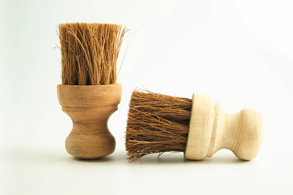Biodegradable washing up brush with bamboo handle and plant-based bristles resting on a wooden countertop next to citrus peels